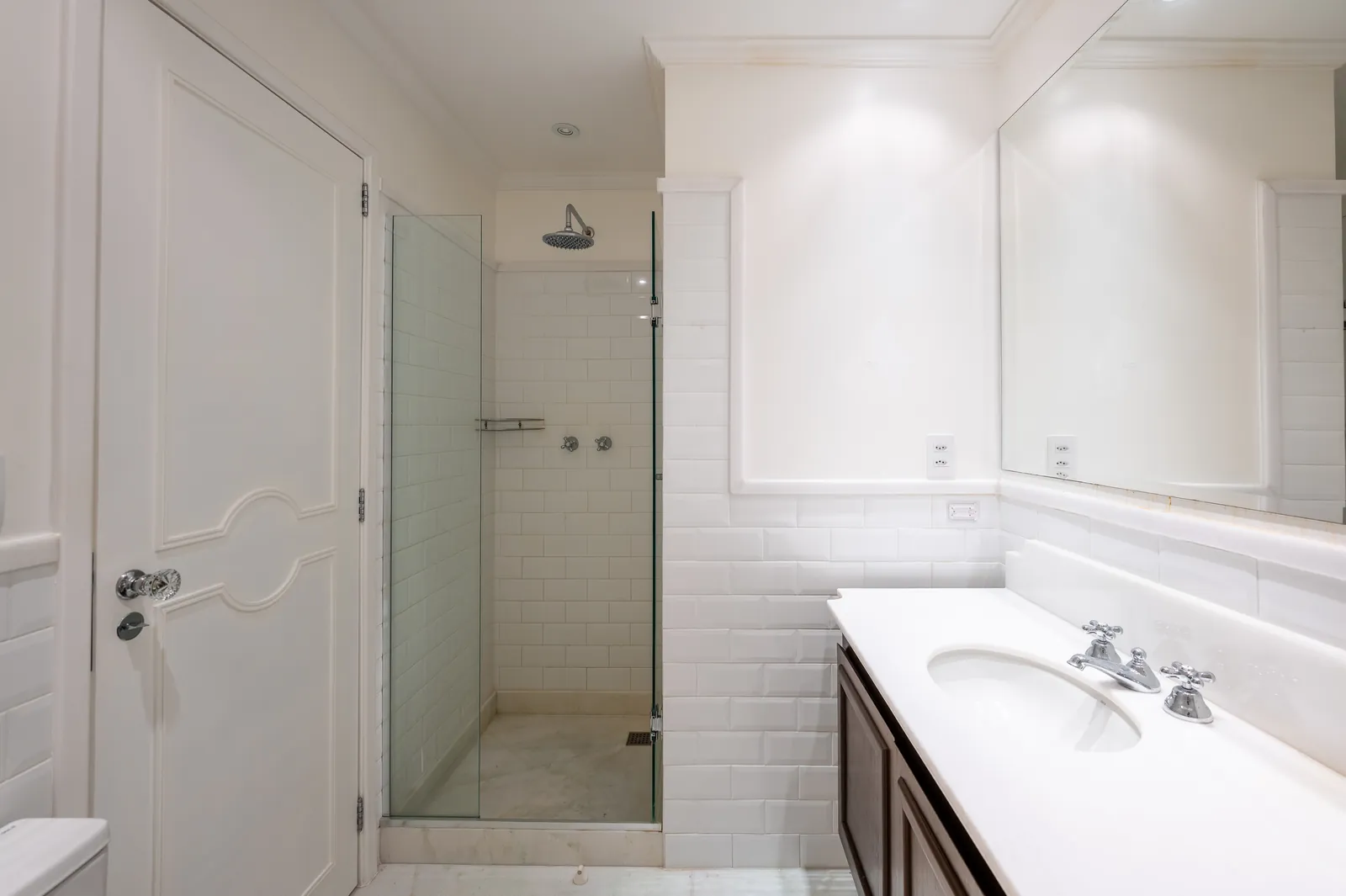 A bathroom with a glass shower, dark-wood vanity and white subway tiles
