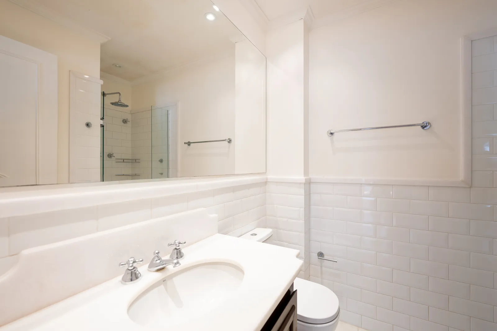 A bathroom with a glass shower, white tiling and a marble vanity