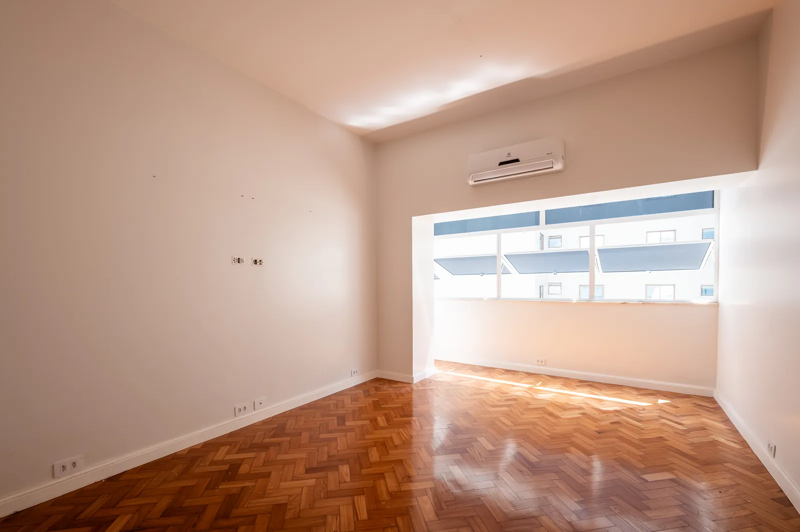 A bedroom with air conditioning, parquet and a window over the city