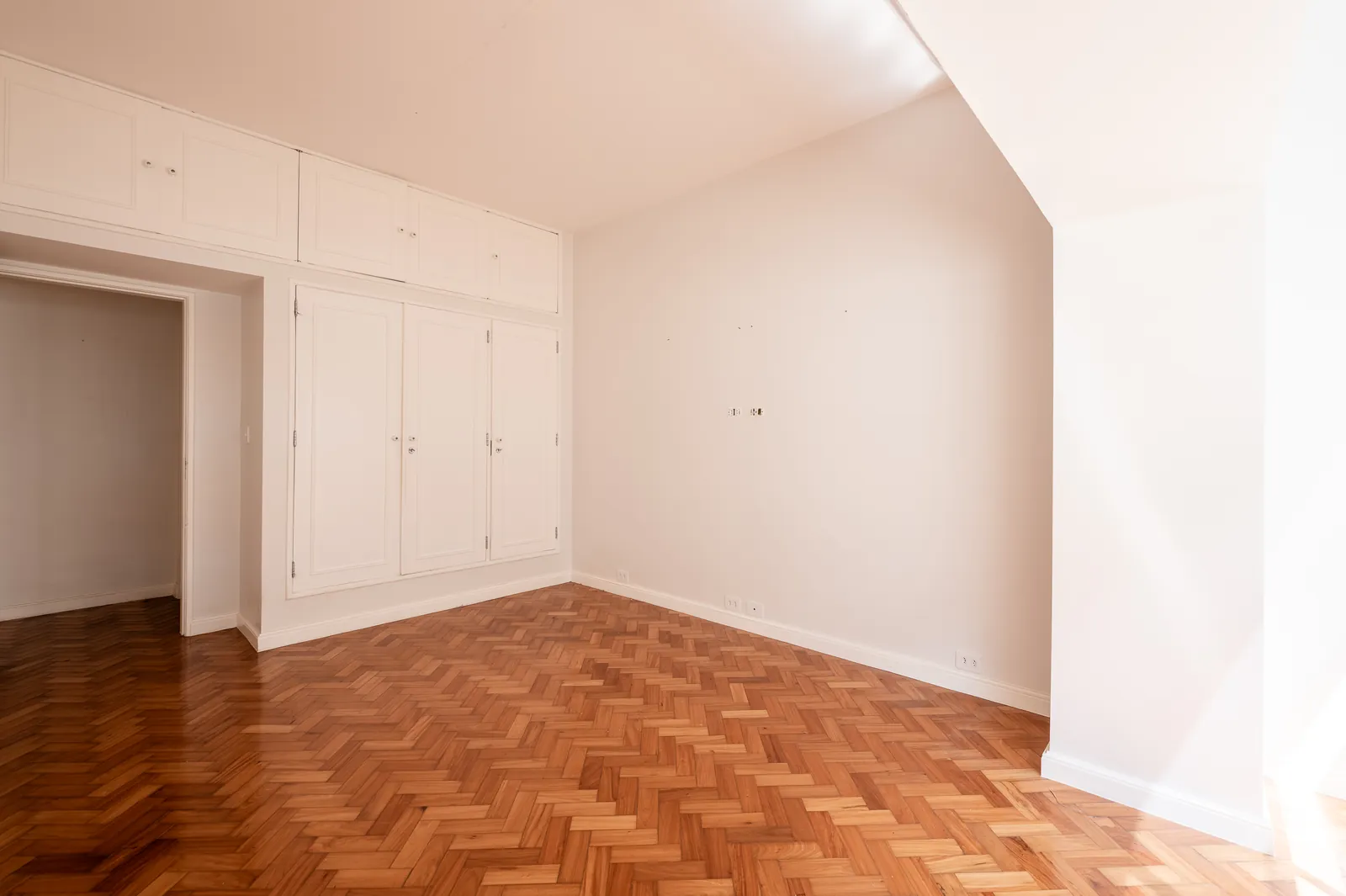 A bedroom with white built-in wardrobes, parquet and a doorway