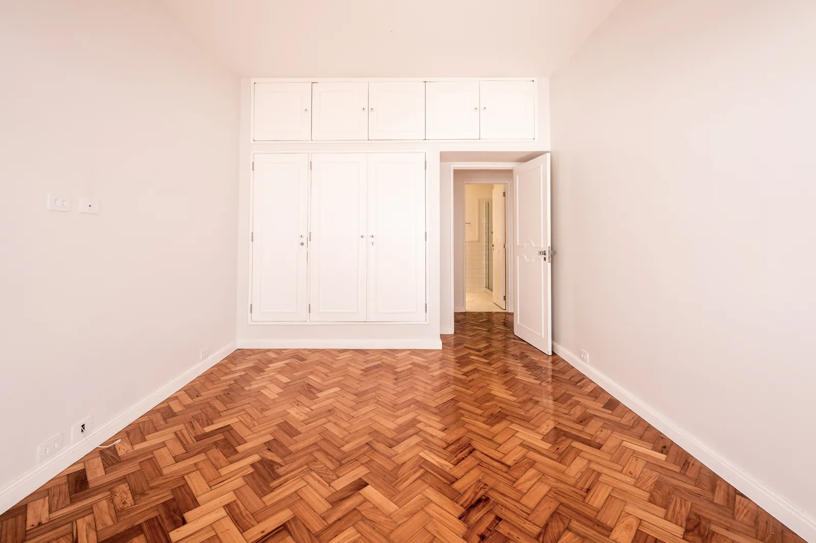 A bedroom with white fitted cupboards and herringbone parquet