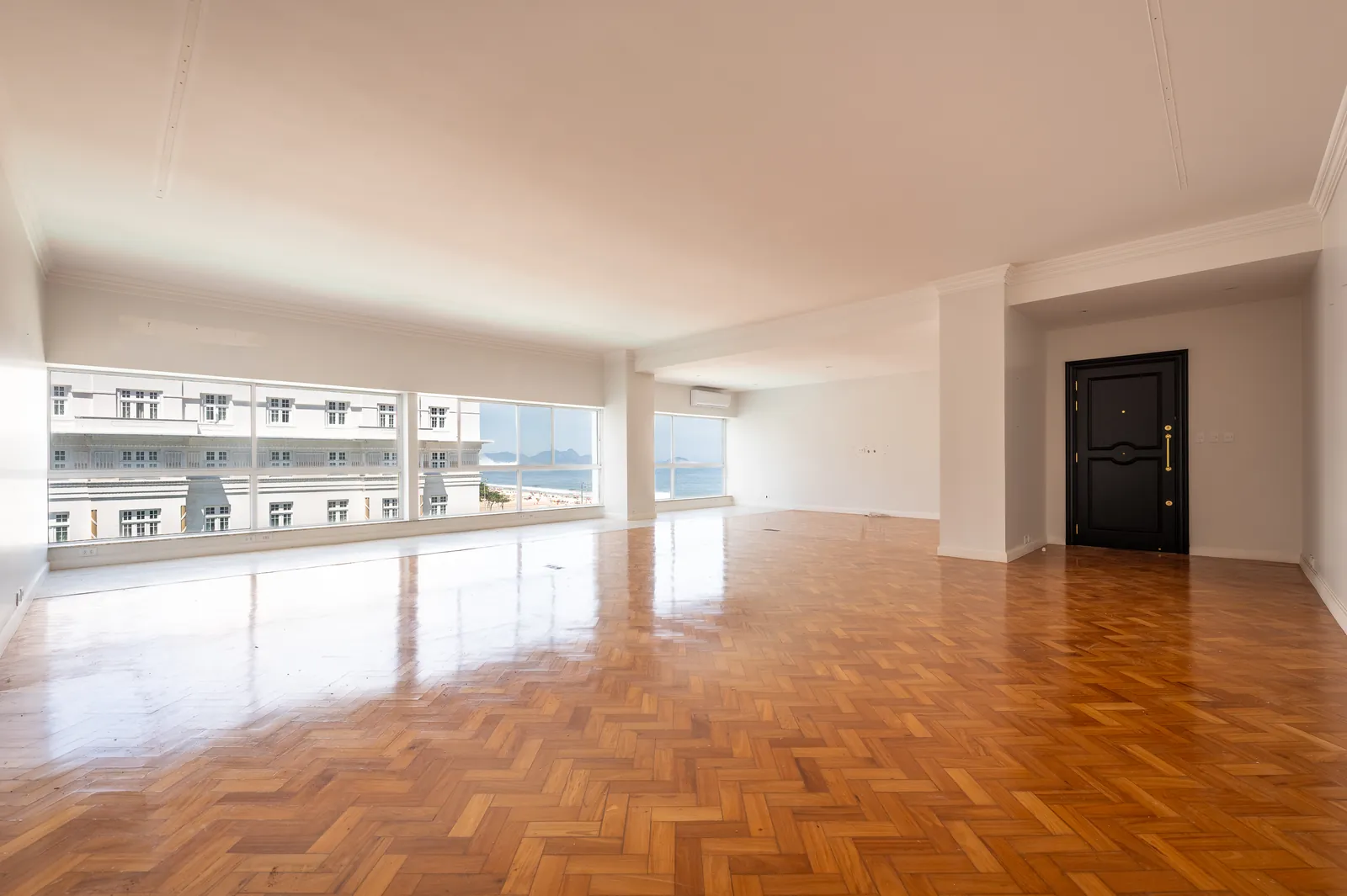 A reception room in herringbone parquet, the glass open to the sea and the entrance door