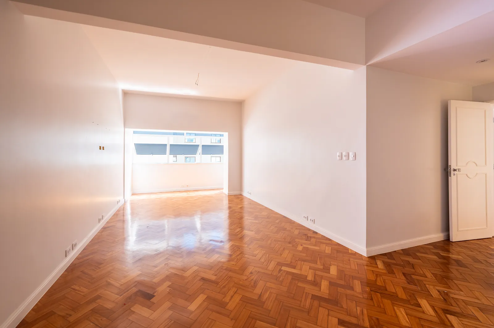 A bright room in herringbone parquet, a tall window and a panelled door